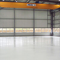 Leere Industriehalle mit einem orangen Hebekran und beschichtetem Boden